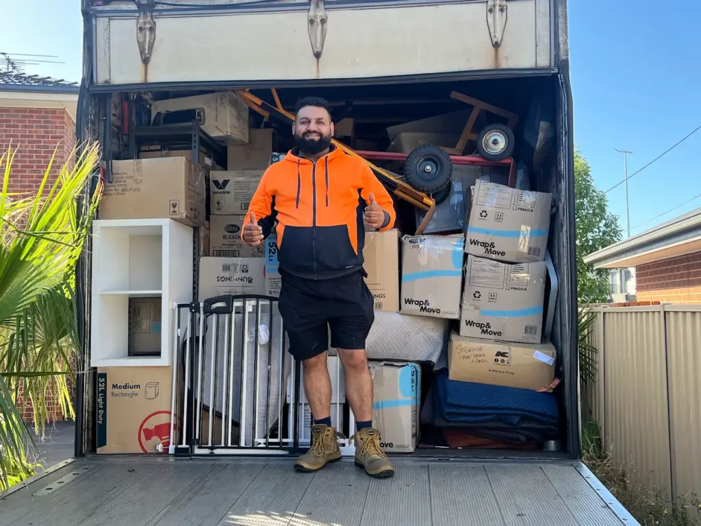 A mover standing in front of a fully loaded truck filled with boxes, furniture, and large items, representing big stuff movers handling careful loading and transport.