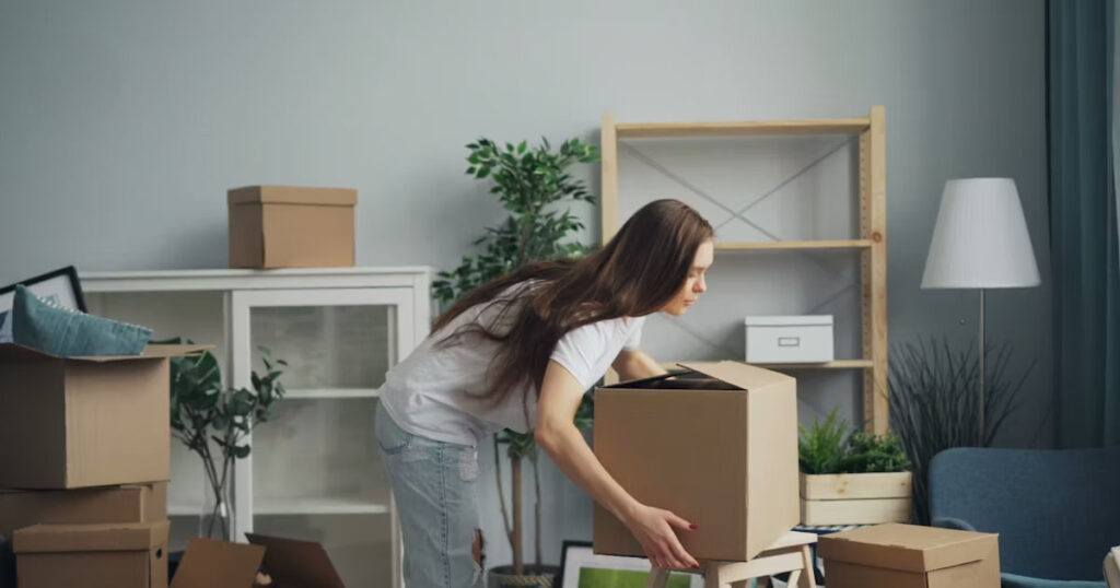Person lifting a cardboard box in a living room during a house move in Australia